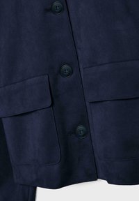 Tmavomodrá semišová bunda s oštyrmi prednými vreckami, dvoma veľkými vreckami s klopou, dvoma guľatými gombíkmi a hladkou textúrou.