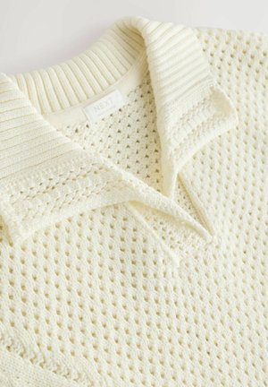 Polo shirt en maille de couleur crème avec un motif texturé en tissage ouvert et un col côtelé. L'étiquette indique "NEXT", fabriqué en Inde.