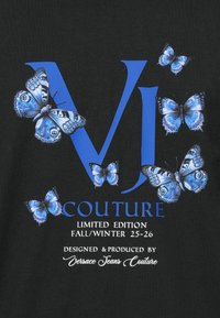 Černé tričko s modře tištěným logem "VJ" a motýly. Text zní "COUTURE LIMITED EDITION FALL/WINTER 25-26" v bílé.