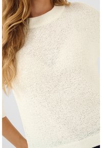 Pull en tricot crème clair avec un col rond et des manches courtes. Présente un motif texturé avec un design lâche et aéré.