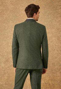 Blazer en laine vert foncé avec une coupe structurée, doté d'un col cranté et de deux boutons, associé à un pantalon assorti. Texture douce.
