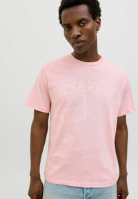 Roze katoenen t-shirt met korte mouwen, ronde halslijn en een voorzijde grafiek met "JACK&JONES" in een vervaagde print. Draagt het met lichtblauwe jeans.