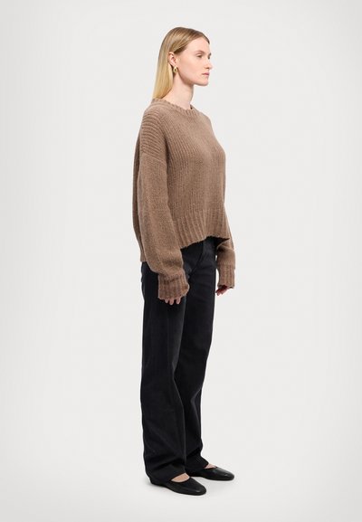 Maglione lavorato a maglia di un marrone chiaro con un design corto e orlo a costine, abbinato a pantaloni neri a gamba larga e ballerine nere. Vista laterale.