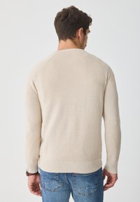 Beige svetr s ribováním a dlouhými rukávy, kulatým výstřihem, s jemnou strukturou a závazným střihem v oblasti pasu a na manžetách.