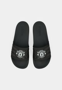 Melnas čības ar teksturētu zolīti, ar gludu siksnu, kas rotāta ar Mančestras United logotipu un Adidas zīmolu.