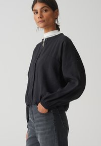 Zwarte button-up shirt met een relaxte pasvorm, lange mouwen en een licht gestructureerde stof. Gecombineerd met donkere denim jeans.