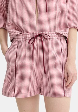 Donna che indossa shorts a quadretti rossi e bianchi con coulisse bordeaux e tasche laterali, abbinati a un top coordinato.