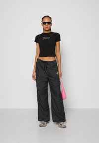 Black crop top with "Juicy" text, black waterproof wide-leg pants, silver sneakers, and a pink handbag. White sunglasses complete the look.