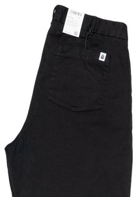 Pantaloni in cotone neri con una tasca posteriore con toppa del logo, vita standard e etichetta di cura attaccata. Texture liscia e opaca.