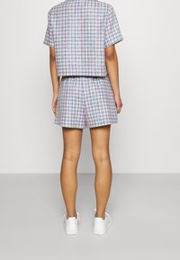 Twee-delig outfit met een kortemouwen, crop-top en bijpassende shorts, beide in een multikleurige ruitpatroon. Gekocht met witte sneakers.
