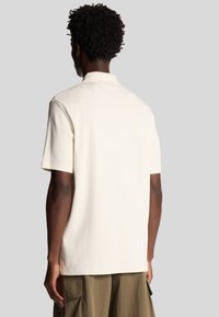 Crème short-sleeve polo shirt van een gestructureerde stof, met een klassieke kraag en een ontspannen pasvorm, gecombineerd met olijfgroene cargobroek.