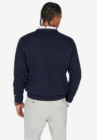 Suder azul marino de punto con textura de canalé y un cuello redondo, combinado con pantalones gris claro. Presenta acentos en los puños cerca de la muñeca.