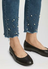 Jean en denim avec des embellissements en perles et en métal à l'ourlet, présentant un bord effiloché. Assortis à des ballerines noires plates.