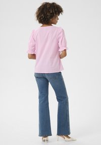 Gaiši rozā blūze ar puffiem piedurknēm, apaļu kakla izgriezumu un drapētiem rokaviem, apvienota ar ziliem platiem džinsiem un gaišas krāsas papēžu kurpēm.