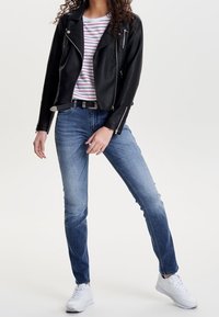 Schwarze Leder-Bikerjacke über einem schwarz-weiß gestreiften T-Shirt, kombiniert mit schmalen blauen Jeans und weißen Sneakers.