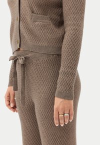 Brun stickad kofta och matchande byxor med ett texturerat diamantmönster, med knyt i midjan och en ficka på koftan.