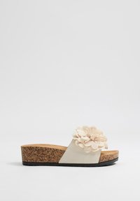 Sandalia de cuña beige con suela de corcho, que presenta un acento de flor texturizada y un diseño de tira suave, ofreciendo un aspecto casual y cómodo.