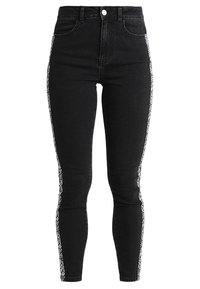 Jeans ajustados negros con una cintura alta, que presentan un patrón floral blanco a lo largo de las costuras laterales y un diseño clásico de cinco bolsillos.