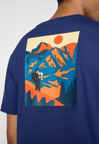 Persoon met een rugzak die een kaart vasthoudt, staat op een oranje heuvelrug tegen een gestileerde achtergrond van blauwe en oranje bergen met de zon en dennenbomen.