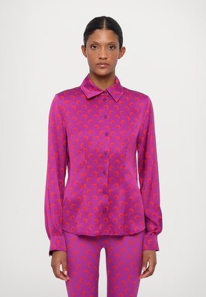 Fuchsia blouse with long sleeves, button-down front, and a repeating crescent moon pattern in orange. Made of smooth, shiny fabric.