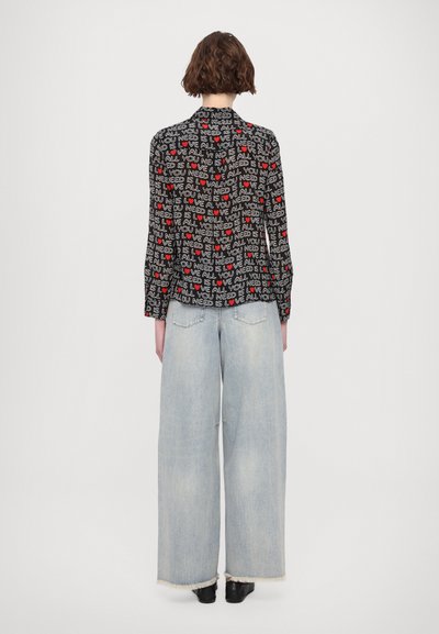 Black shirt with white and red text pattern, featuring long sleeves. Paired with light blue wide-leg jeans with frayed hem. Black shoes.