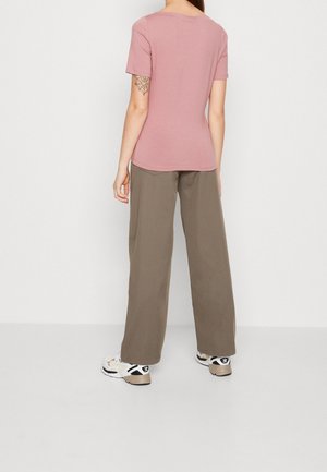 Maglietta rosa a maniche corte realizzata in tessuto morbido, abbinata a pantaloni larghi verde oliva e sneakers bianche chunky.