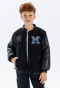 Giacca varsity nera con corpo in lana e maniche in pelle nera lucida, dotata di una grande "M" blu ricamata e dettagli testuali sul fronte.