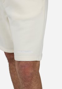 Lys beige shorts lavet af blødt stof med et enkelt design. Mærket "PEGADOR" er broderet i hvidt på kanten.