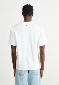 Vit bomull t-shirt med en liten svart logotyp på övre delen av ryggen, korta ärmar och en avslappnad passform, kombinerad med ljusblå denimshorts.