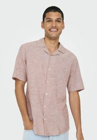 Camisa de manga corta con cuello en un tejido texturizado de color rosa claro, con un patrón sutil, que presenta botones blancos y un corte relajado.