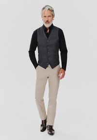 Grafitowa kamizelka na czarnej koszuli, zestawiona z beżowymi spodniami i ciemnobrązowymi butami, z dopasowanym krojem i detalami w postaci guzików.