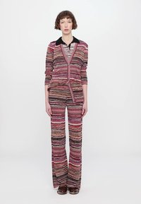 Tutina lavorata a maglia con un motivo a strisce multicolori nei toni del rosa, nero e crema. Presenta un colletto e pantaloni svasati.