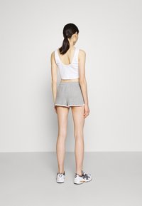 Top cropped bianco e pantaloni grigi con bordi bianchi. La modella indossa scarpe da ginnastica e ha capelli lunghi raccolti in una coda di cavallo.