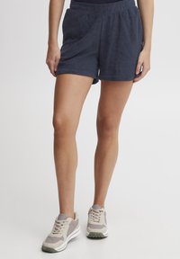 Marineblå, bomullsterry shorts med elastisk livlinje og sidelommer. Kombinert med beige og grå treningssko.