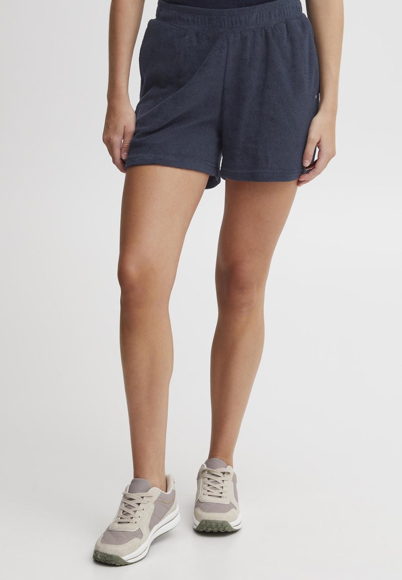 Marineblå, bomullsterry shorts med elastisk livlinje og sidelommer. Kombinert med beige og grå treningssko.