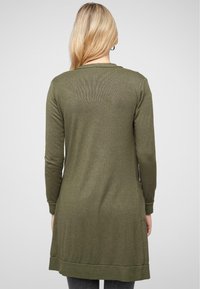 Pitkä oliivinvihreä neuletakki, joka on valmistettu pehmeästä kankaasta. Siinä on ribbikuvioitu helma, pitkät hihat ja sivutaskut; minimalistinen muotoilu ilman kuvioita.