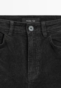 Černé manžestrové kalhoty s knoflíkovým zapínáním, které mají texturovaný vertikální proužkovaný vzor a štítek "Massimo Dutti" na pase.