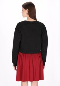 Fekete, hosszú ujjú, kerek nyakú, rövidített pulóver, bordó redős szoknyával, amely középmagasan ér le.