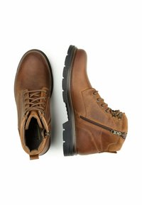 Brązowe skórzane buty trekkingowe z sznurowanym przodem i suwakiem z boku. Gruba czarna gumowa podeszwa oraz teksturowane detale powierzchni.