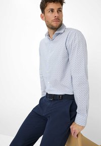 Lichtblauw overhemd met een marineblauw en wit gestippeld patroon, gecombineerd met marineblauwe broek en een geweven riem. Gladde stoftextuur.