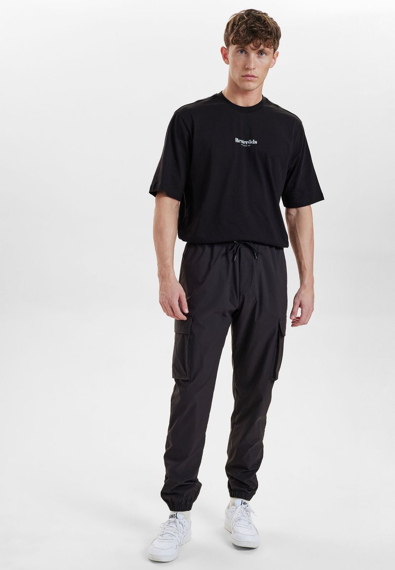 Zwarte t-shirt met korte mouwen en logo, gecombineerd met zwarte cargo pants met zijzakken en elastische boorden, gedragen met witte sneakers.
