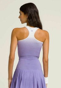 Top corto atlético morado con textura acanalada, ribete degradado blanco y detalles del logo. Combinado con una falda plisada, que resalta un diseño ajustado.