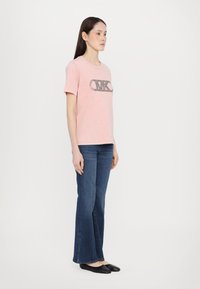 Rosa bomull T-skjorte med korte ermer og rund hals, med en svart logo-design. Kombinert med mørkeblå utsvingte bukser og svarte sko.