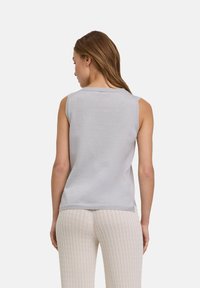 Top senza maniche grigio chiaro con scollatura rotonda, texture liscia e spacchi laterali, abbinato a pantaloni in maglia crema texture.