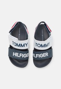 Niebieskie i białe sandały z regulowanymi paskami. "TOMMY" wydrukowane na białym pasku górnym oraz "HILFIGER" na dolnym pasku. Gumowa podeszwa.