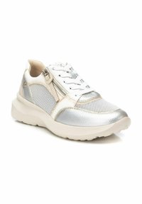 Zapatilla metálica plateada y blanca con paneles de malla texturizada, cierre de cordones y cremallera, cuello acolchado y una suela blanca gruesa.