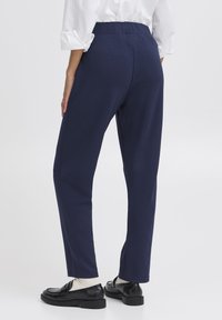 Pantaloni blu navy in tessuto elastico, taglio slim con una texture liscia, dotati di una vita alta e senza tasche visibili.