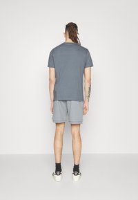 Grå kortärmad t-shirt i kombination med grå shorts. Tyget verkar mjukt. Personen bär svarta strumpor och skor med beige detaljer.