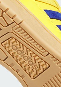 Semelle de basket Adidas jaune avec un motif en caoutchouc texturé et des rayures en suède bleu sur la partie supérieure de la chaussure.