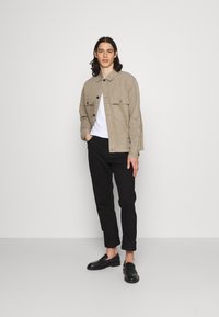 Chaqueta de ante beige con bolsillos frontales, camiseta blanca, pantalones negros ajustados y mocasines negros. Diseño minimalista, colores neutros, estilo versátil.